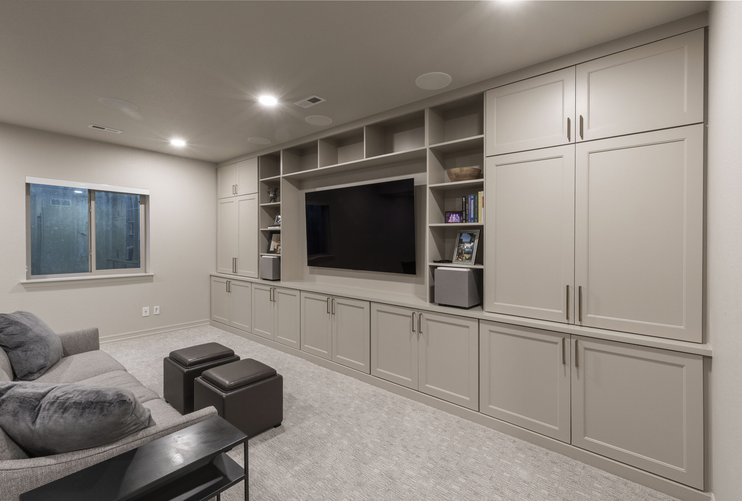 Basement home theater with built-in cabinets, a large TV, and a sofa, highlighting a functional and well-designed entertainment area.