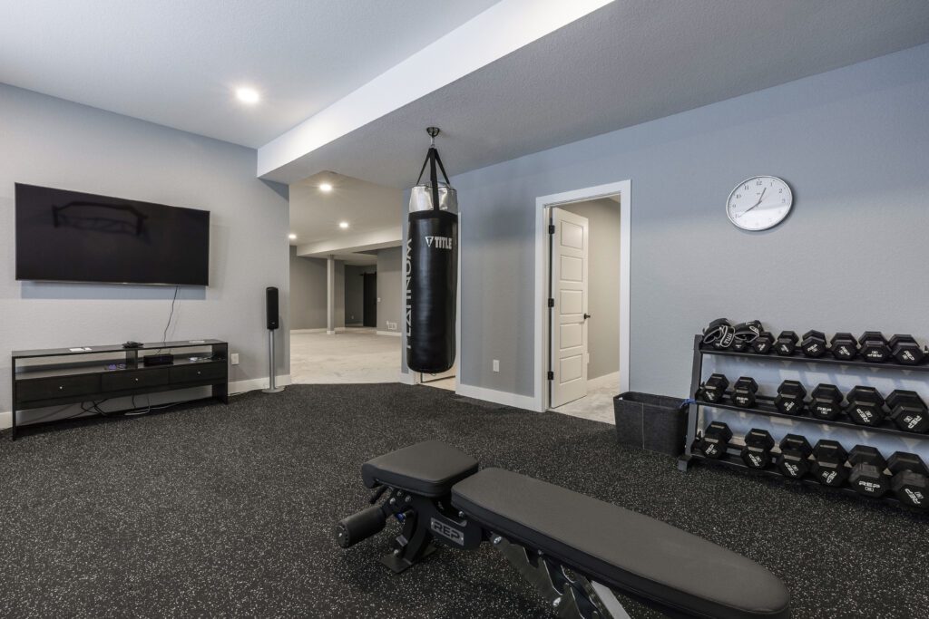 Elkstone Basements Home gym with a punching bag, weight rack, bench, and TV, showcasing a modern basement renovation.